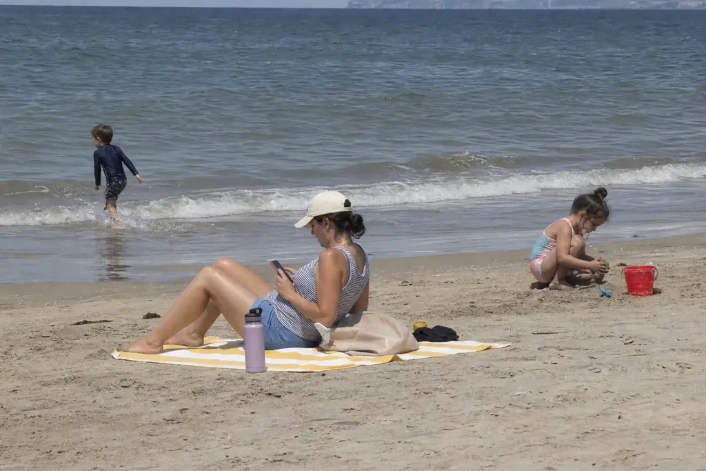 Familj på stranden som planerar semester med familjen på sitt eget vis, barn leker i vattnet och i sanden.